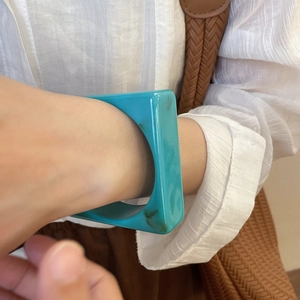 Detail of square resin bangle in green marble finish worn on wrist with woven bag strap