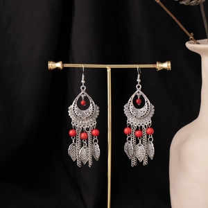 Detail of bohemian drop earrings with red beads and leaf-shaped tassels on a gold stand