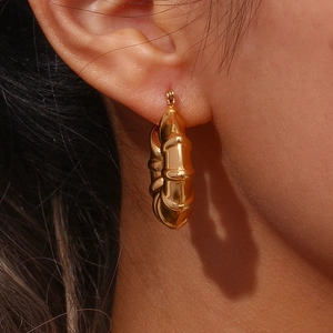 Close-up of golden bamboo texture hoop earring worn on a model ear with glossy finish