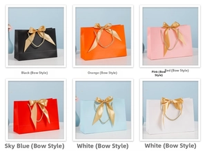 Macro detail of various colored gift bags featuring gold satin bows and woven handles