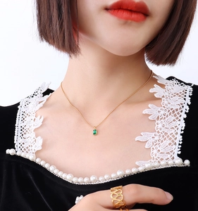 Detailed close-up of emerald zircon necklace and hollow geometric gold ring on a model