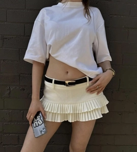 Detalle de minifalda blanca plisada a capas con cinturón negro y textura de volantes