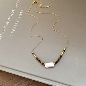 Detail of tiger eye stone and baroque pearl pendant on a gold chain necklace