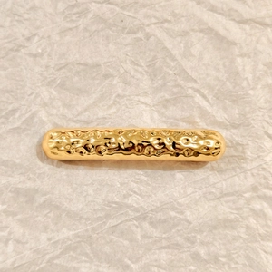 Detailed view of golden spring hair clip with irregular texture on white paper background