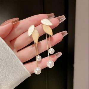 Detail of leaf-shaped tassel earrings with white pearls and gold chains held in hand