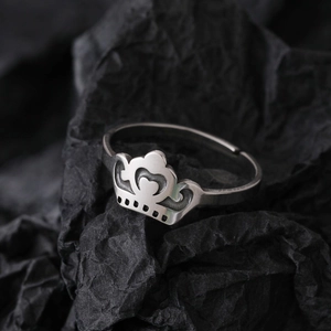 Luminous silver stainless steel crown ring with heart pattern on black paper backdrop