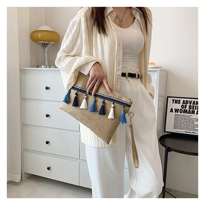 Detail of straw woven envelope clutch featuring blue and white tassel with a wrist strap