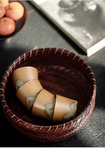 Detail of four ceramic kung fu teacups with mountain patterns in a woven bamboo basket