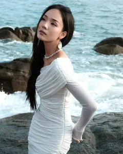 Detail of elegant white off-shoulder ruched dress with long sleeves in a coastal setting