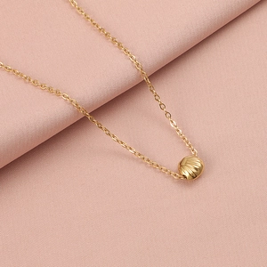 Close-up of a golden shell pendant on a fine chain over soft pink textured fabric