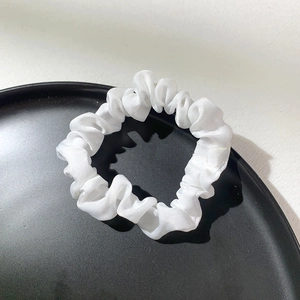 Detail view of a white satin scrunchie with smooth texture in a black matte display tray
