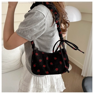 Detail of black corduroy hobo bag featuring red strawberry embroidery and bow detail