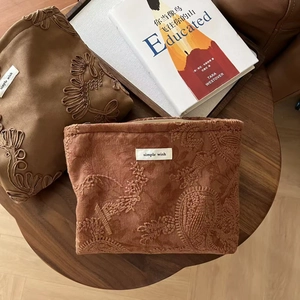 Macro shot of embroidered camel suede pouches next to a book on a wooden table