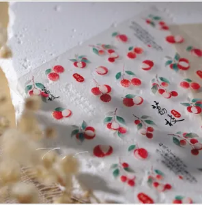 Close-up of glittery lychee nail art stickers with leaves and seals on stone surface