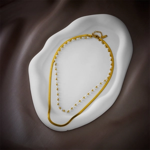 Double-layered gold flat snake chain necklace with white beads on a ceramic tray
