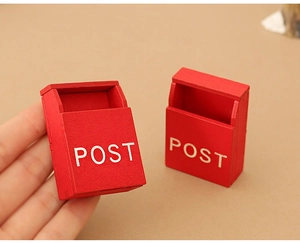 Close-up of a hand holding a miniature red wooden dollhouse mailbox with white POST text