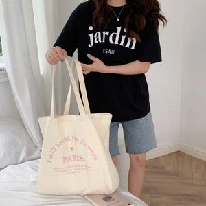 Detail of a beige canvas tote bag with pink PARIS flower text on a casual lifestyle setting
