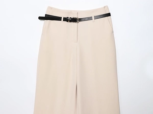 Detail of high-waisted beige trousers featuring a slim black leather belt and metal buckle