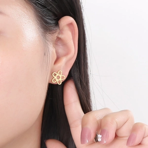 Close-up of elegant gold hollow flower stud earring worn on model against white backdrop