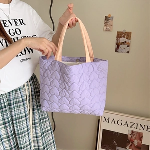 Purple quilted heart tote bag with pink handles shown in a lifestyle scene with model