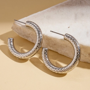Close-up of silver C-shape metal hoop earring with irregular hammered texture on stone