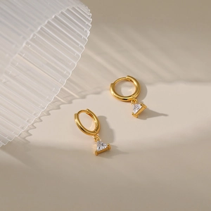 Detail of gold-plated hoop earrings with triangle zircon pendants and striped light shadows