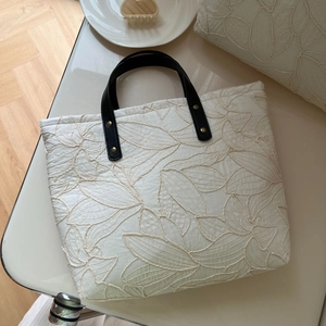Macro view of beige quilted tote bag showing intricate leaf embroidery and leather handles