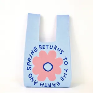 Close-up of light blue knitted tote bag with pink flower and spring letter pattern
