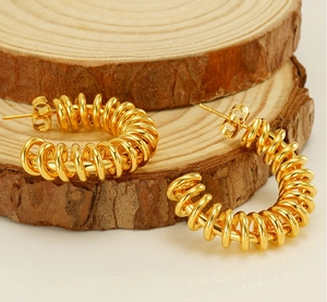 Detailed view of gold C-shaped spring earrings on wooden blocks with metallic finish