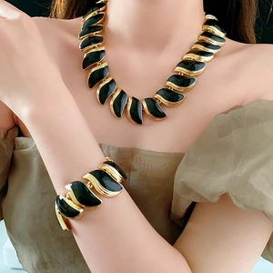 Détail rapproché du collier et bracelet dorés en forme de feuilles avec émail noir