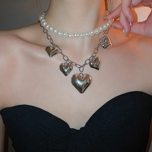 Detail of layered necklace featuring white pearls and silver heart pendants on a model