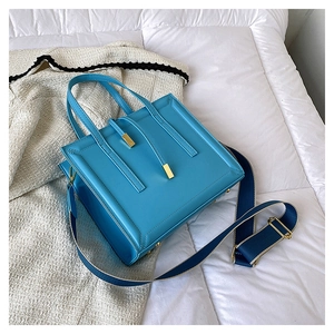 Detail of blue crossbody bag with gold hardware and wide woven strap on soft bedding