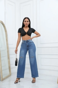 Detail of high-waist distressed wide-leg jeans with knee cut-outs and a black crop top