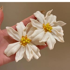 Close-up of white acrylic flower earrings with yellow stamen held by hand