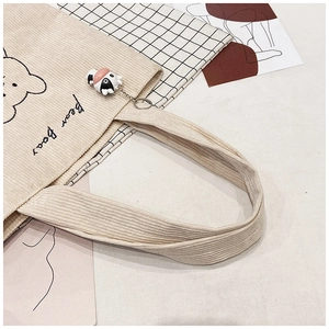 Detailed close-up of corduroy tote bag featuring bear embroidery and cow plush keychain