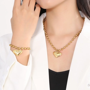 Close-up of a gold heart pendant necklace and matching bead bracelet set worn by a model