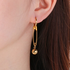 Detailed close-up of golden safety pin earring with polished metal bead on a model