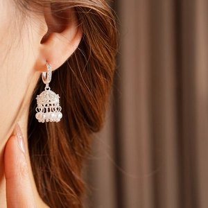 Detail of silver bell earring with zircon inlay and hanging pearls on model's ear