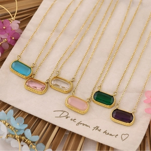 Flat lay of colorful rectangular zircon pendants on gold chains over beige fabric