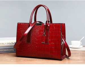 Macro detail of red crocodile pattern patent leather tote bag on wooden desktop