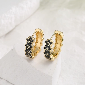 Gold-plated hoop earrings with black enamel flower pattern on a marble base