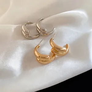 Golden and silver C-shaped teardrop earrings on white silk background with high polish finish