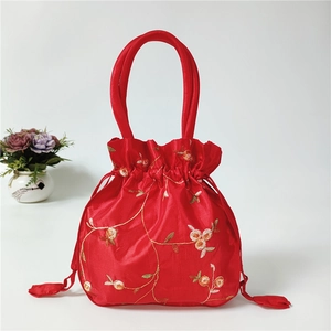 Detailed close-up of red satin drawstring bag with gold floral embroidery and tassels