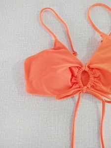 Detail of orange bikini top with central metal ring and ruched fabric texture