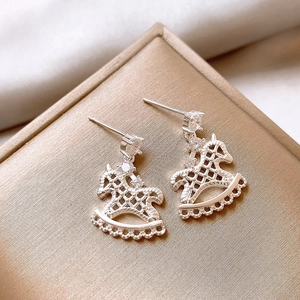 Macro shot of silver rocking horse earrings with cubic zirconia on gold silk gift box