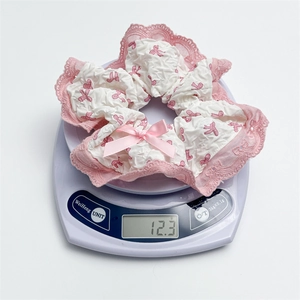 Lace scrunchie with pink bow showing weight of 12.3g on a digital electronic scale