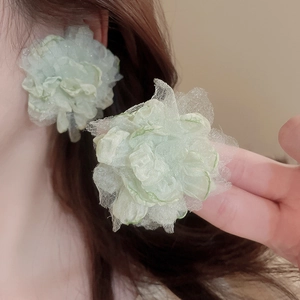 Close-up of light green lace flower earrings worn by a model with delicate petals