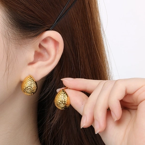 Macro detail of gold teardrop earrings featuring a unique hammered textured finish