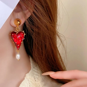 Close-up of red heart earrings with gold trim and a hanging white pearl on model