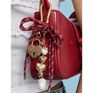 Close-up of golden heart padlock and baroque pearl charm on a red leather handbag